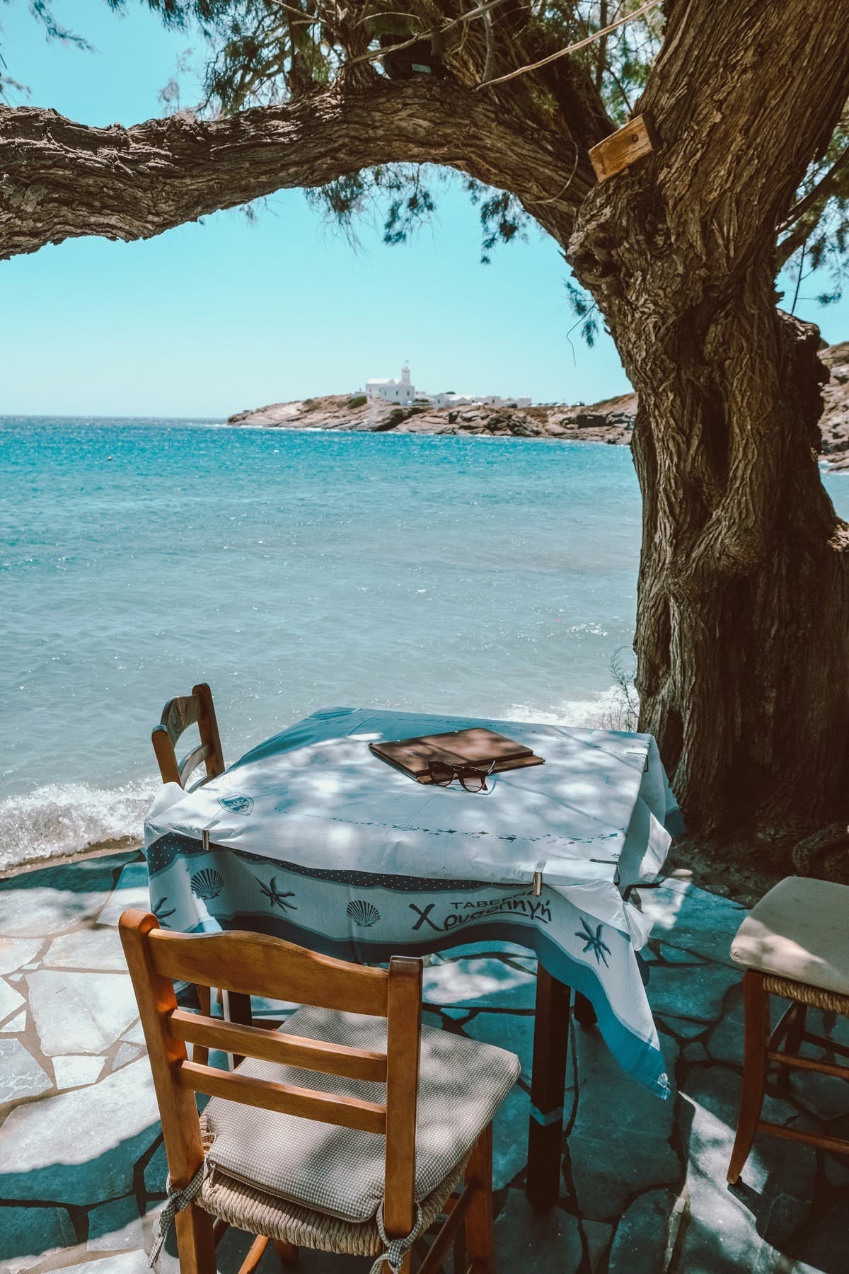 A taverna table under a tree right by the sea on Sifnos