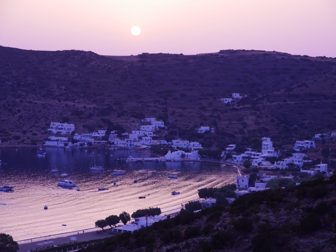 Vathi bay in violet dusk light with the moon over the ridge and white houses by the water